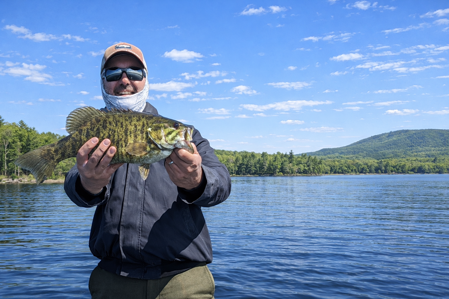 Angler holding a trophy smallmouth bass during a Bar Harbor fishing charter on a scenic Maine lake