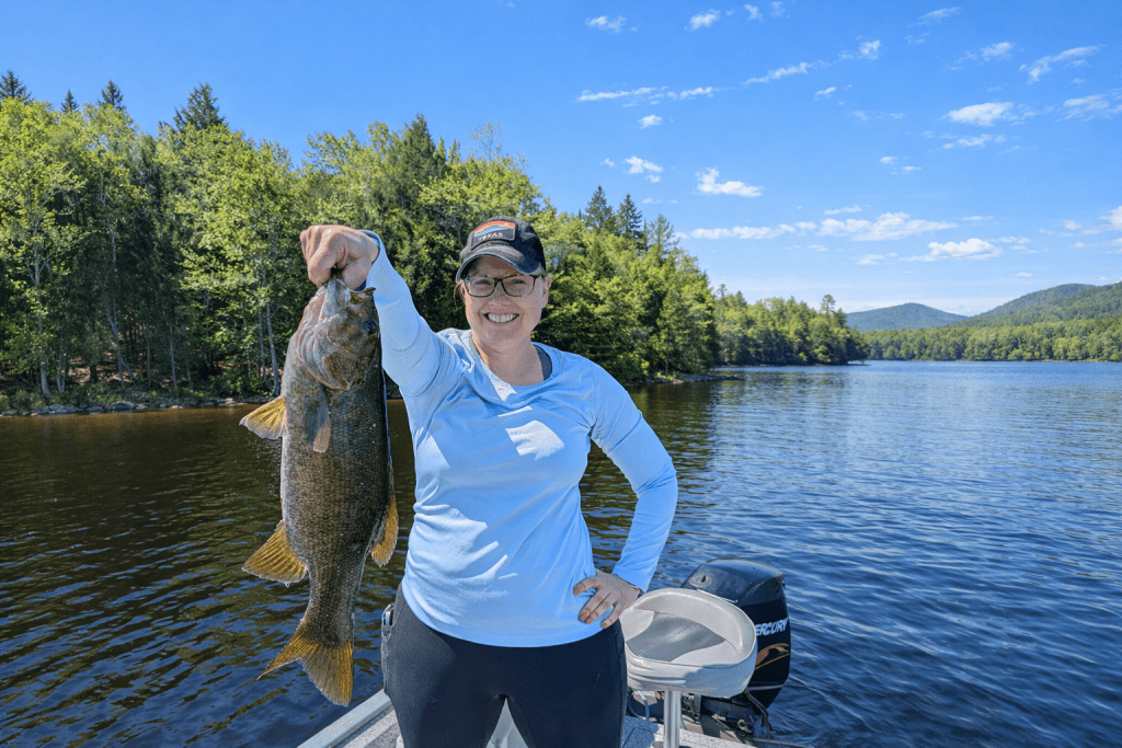 Smiling angler holding a large smallmouth bass on a guided freshwater fishing trip near Bar Harbor, Maine